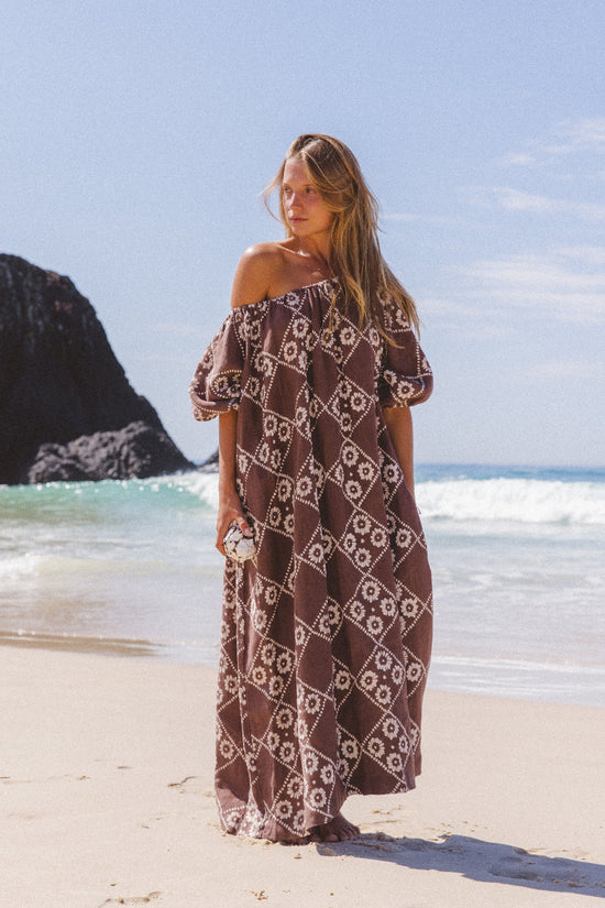 Dahlia Maxi Dress Maple — full length standing at coastal beach, off-shoulder billowy sleeves, hand block print linen with rocky headland backdrop | Daughters of India