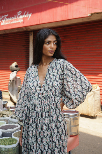Bhoomi Maxi Dress Onyx — upper body close-up at Indian spice market, onyx hand block print V-neckline and long sleeve detail, red shutters and spice stall background India | Daughters of India