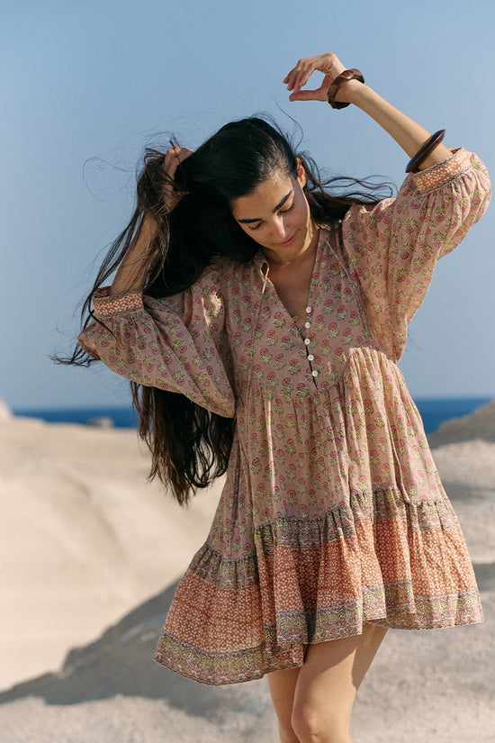 Woman dancing on beach sand wearing the Daughters of India Bhoomi Mini Dress in Sunset, arms raised with flowing hair, showcasing the voluminous tiered skirt