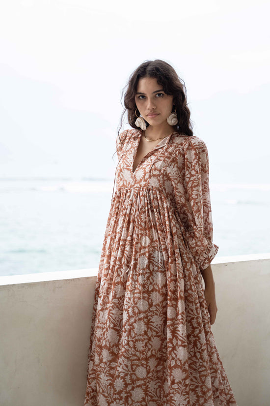 Daughters of India Kyra Midi Dress in Caramel — standing by veranda wall with ocean behind, gathered waist detail