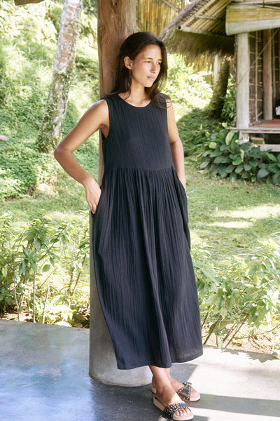 Nadi Dress Black — full length on tropical veranda, black double gauze cotton midi dress with flowing silhouette, bamboo railing and lush greenery | Daughters of India