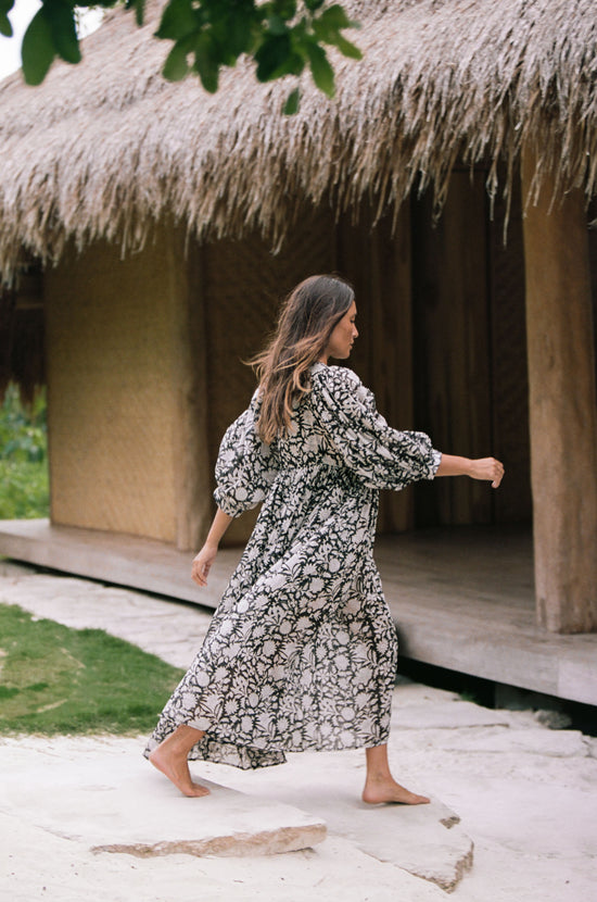 Daughters of India Kyra Maxi Dress in Pepper — back view walking past thatched hut, billowed sleeves, gathered waist