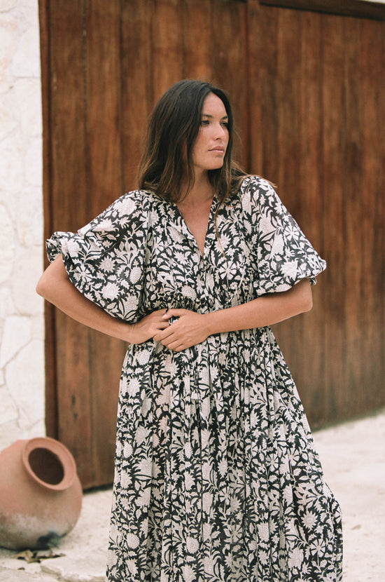 Daughters of India Kyra Maxi Dress in Pepper — upper body by wooden door, billowed sleeves spread, terracotta pot