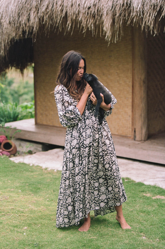 Daughters of India Kyra Maxi Dress in Pepper — holding puppy by thatched hut, V-neckline and billowed sleeves